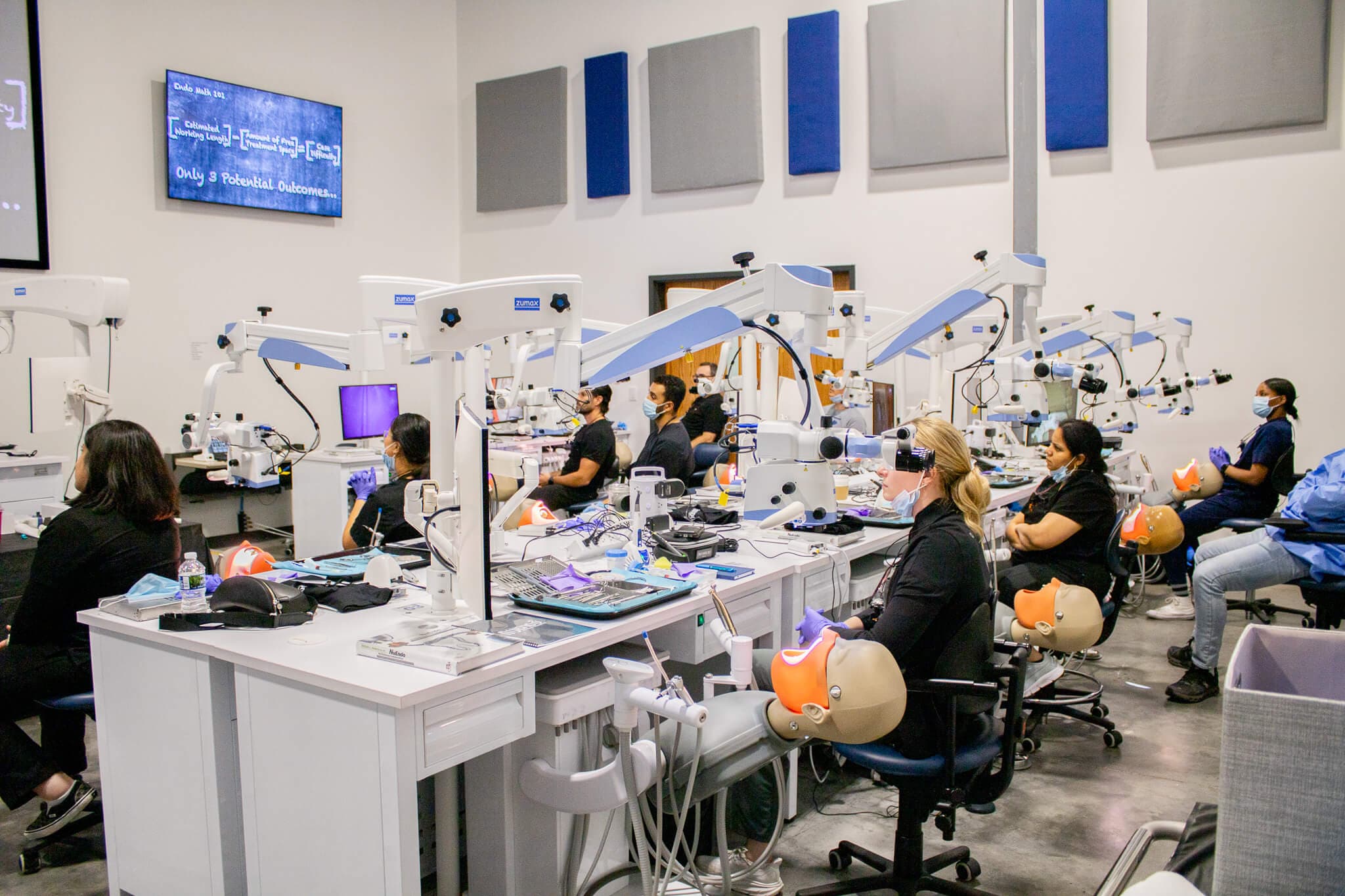 The training floor at the Enova Dental Microscopic Training Center — rows of operatories, each with its own dental operating microscope and manikin head, with course participants working at their stations